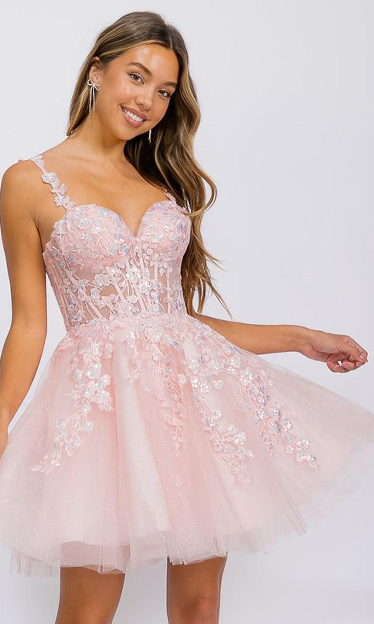 A woman wears the Short Fit-and-Flare Lace Hoco Dress: Eureka EK152, featuring a light pink embroidered lace bodice and flared tulle skirt, standing against a plain light background.